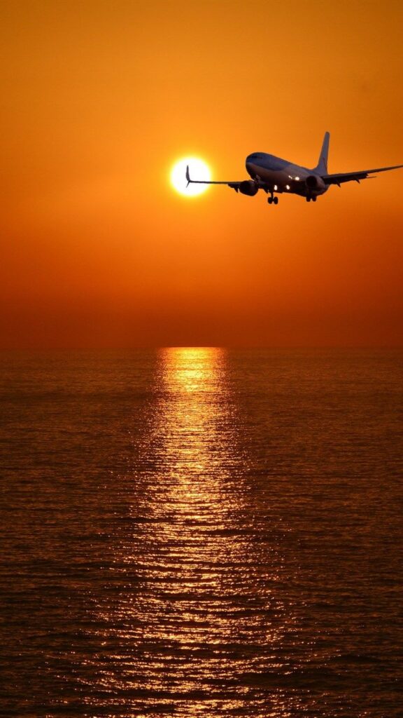 papel de parede para celular de avião voando por cima de um mar com o sol se pondo