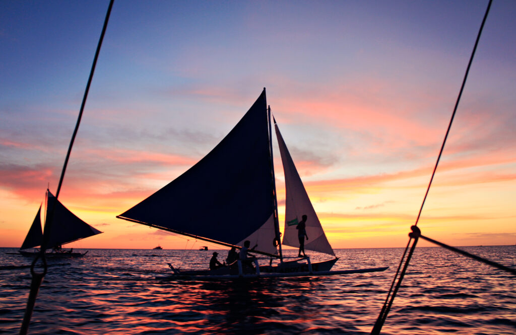 barco velejando na praia com lindo por de do sol ao fundo nesse wallpaper para pc